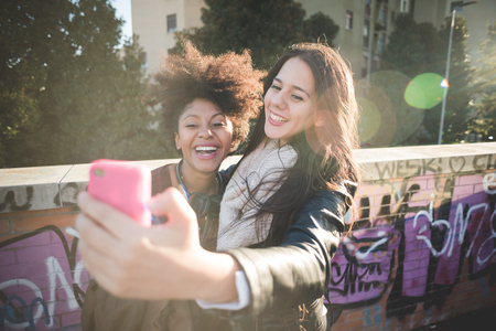 two multiethnic beautiful young woman black and caucasian having fun taking selfie in townの写真素材