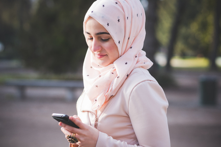 young beautiful muslim woman at the park in spring using smartphone connected online wirelessの写真素材
