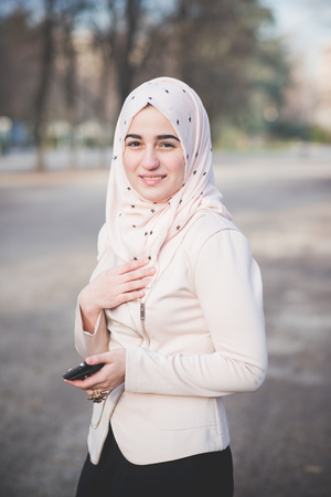 young beautiful muslim woman at the park in spring using smartphone connected online wirelessの写真素材