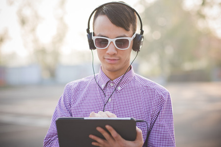 young crazy funny asian man in town outdoor lifestyle listening music with headphones and tabletの写真素材