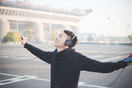 young crazy funny asian man in town outdoor lifestyle listening music with headphonesの写真素材