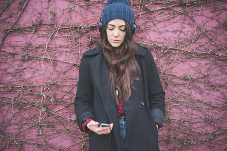 young beautiful long hair model woman living the city in winter outdoor city listening to music with headphonesの写真素材