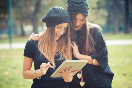 young couple beautiful women girls autumn using tablet outdoorの写真素材