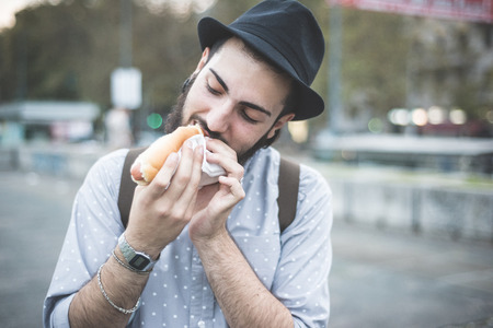 young handsome hipster gay modern man eating hot dog in townの写真素材