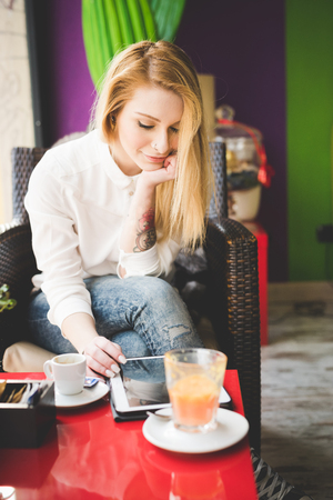 young beautiful blonde straight hair woman in the city sitting at the restaurant using tablet connected onlineの写真素材