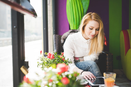 young beautiful blonde straight hair woman in the city sitting at the restaurant using tablet connected onlineの写真素材
