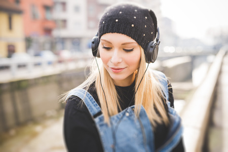 young beautiful blonde straight hair woman in the city with headphones listening to musicの写真素材