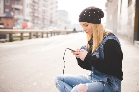 young beautiful blonde straight hair woman in the city using smartphone connected online sitting in the groundの写真素材