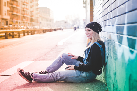 young beautiful blonde straight hair woman in the city using smartphone connected online sitting in the groundの写真素材