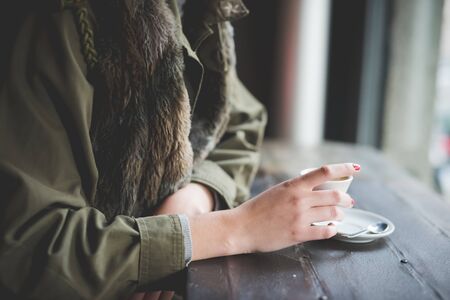 close up of woman hand holding a cup of coffee sitting at the bar in front of windowの写真素材