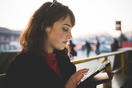 young beautiful red dressed vintage hipster woman in street town using tabletの写真素材
