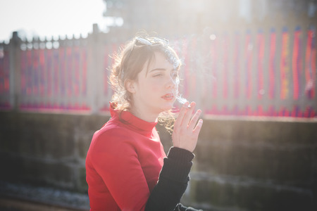 young beautiful red dressed vintage hipster woman at the station smoking cigaretteの写真素材