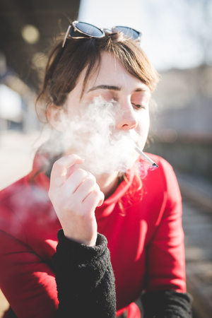 young beautiful red dressed vintage hipster woman at the station smoking cigaretteの写真素材