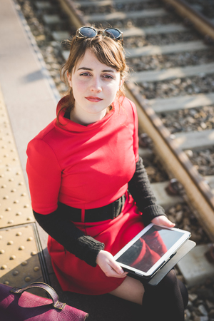young beautiful red dressed vintage hipster woman at the station using tabletの写真素材