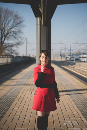young beautiful red dressed vintage hipster woman at the station smoking cigaretteの写真素材