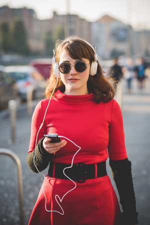 young beautiful red dressed vintage hipster woman in street town listening music with headphonesの写真素材