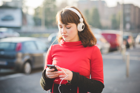 young beautiful red dressed vintage hipster woman in street town listening music with headphonesの写真素材