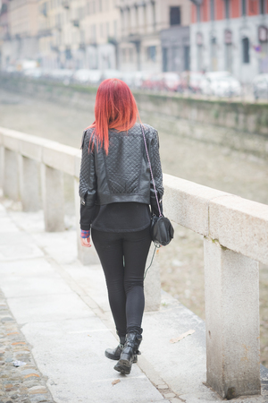 young beautiful red hair venezuelan woman lifestyle in the city of milan outdoor street listening music with headphonesの写真素材