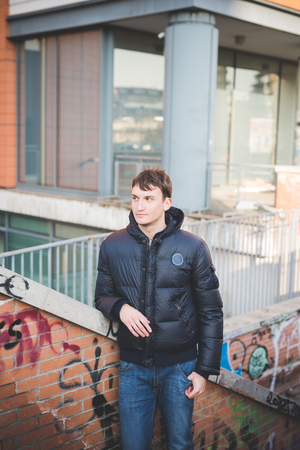 young handsome man in the city leaned on a handrail. He is wearing blue jeans and a blue jacket.の写真素材