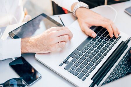 Close up on the hands of a young handsome businessman using technological devices like notebook, smartphone and tablet - communication, business, working conceptの写真素材