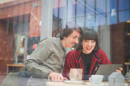 Couple of young beautiful caucasian man and woman business colleague seated on a bar using tablet and smartphone - technology, business, communication conceptの写真素材
