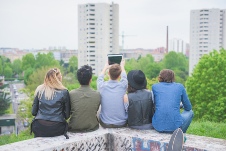 Group of young multiethnic friends sitting in a small wall, seen from behind, looking at the horizon - future, prospective, friendship conceptの写真素材