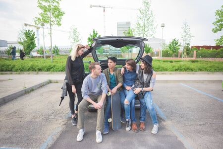 Group of young multiethnic friends sitting in a trunk of a car, talking to each other, having fun - friendship, relax conceptの写真素材
