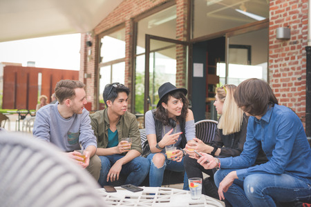 Group of young multiethnic friends sitting in a bar having a drink, talking to each other, having fun - happy hour, friendship, relax conceptの写真素材