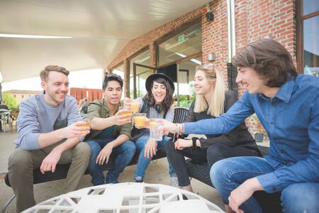 Group of young multiethnic friends sitting in a bar making a toast with beers, having fun - relaxing, happy hour, friendship conceptの写真素材
