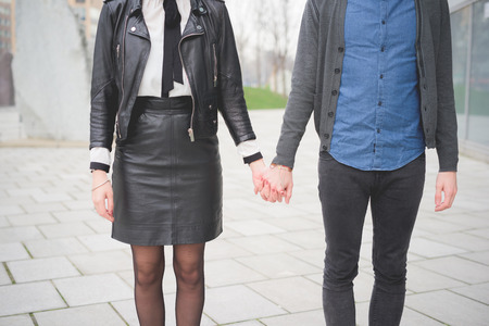 Cropped front view of young caucasian man and woman posing in the streets of the city hand in hand- carefreeness, friendship, love, youth conceptの写真素材