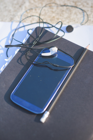 Close up on a smartphone, leaning on a sketchbook, with pencil and earphones beside it - technology, creativity, music conceptの写真素材