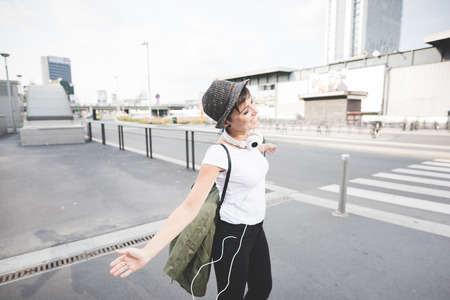 Knee figure of young handsome caucasian brown straight hair woman dancing with arms wide open and headphones around her neck through the street of the city, smiling - feeling free, freedom, dancing conceptの写真素材