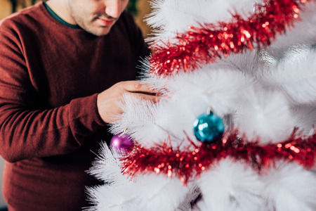 Close up on the hands of couple of young handsome caucasian man decorating christmas tree, looking downward, smiling - christmas, holiday, winter conceptの写真素材