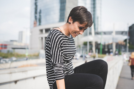 young handsome caucasian brown straight hair woman  sitting on a small wall, looking downward, laughing - serene, carefree conceptの写真素材