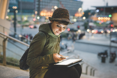 Half length of young handsome caucasian brown straight hair woman using smartphone and tablet, looking downward screen, smiling, face illuminated by screen light - multitasking, technology conceptの写真素材
