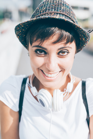 Portrait of young handsome caucasian brown straight hair woman with headphones around her neck, looking in camera, smiling - music, relax, happiness conceptの写真素材