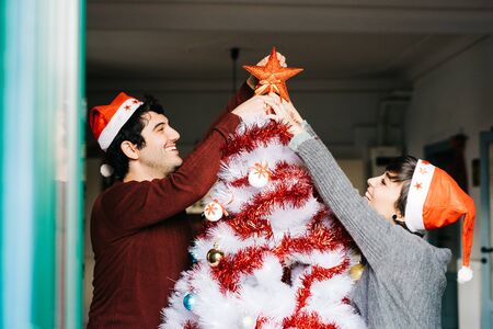 Half length of couple of young handsome caucasian man and woman decorating christmas tree, putting tree topper star - christmas, holiday conceptの写真素材
