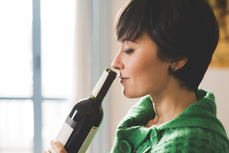 Portrait of young handsome caucasian brown hair woman smelling a bottle of red wine like a sommelier, eyes closed - beverage, happy hour conceptの写真素材