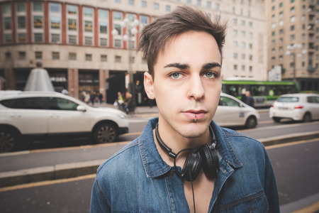 Half length portrait of young handsome alternative dark model man in town with headphones around his neck, looking in camera, pensive - thoughful, serious conceptの写真素材
