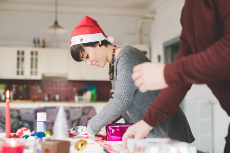 Half length of young handsome caucasian man and woman couple wrapping christmas present with wrapping paper and ribbon, both looking downward - focus on the girl - christmas, couple, holiday conceptの写真素材