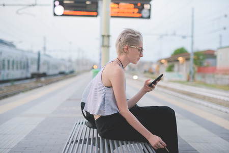 young handsome caucasian blonde italian designer sitting on a bench in railway station, using...