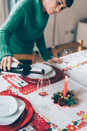 Half length of young handsome caucasian brown hair woman pouring a glass with red wine on a table set for christmas - happy hour, beverage, relax conceptの写真素材