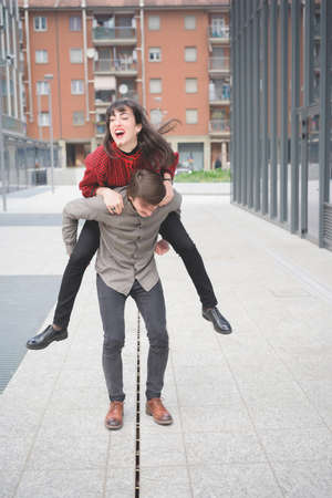 Couple of beautiful woman and man, with mustache, walking through the streets of the city hugging, playing and chatting- freshness, youth, carefree conceptの写真素材