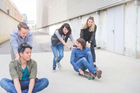 Group of young multiethnic friends having fun laughing, and smiling, racing sitting on their skateboard - friendship, fun conceptの写真素材