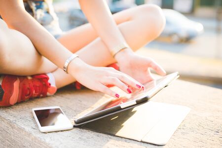 close up on the hands of a woman sitting on a small wall, leg crossed, using smartphone and tablet, scrolling and tapping the screen - technology, multitasking, social network conceptの写真素材