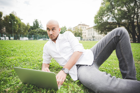 Young handsome caucasian business man sitting in a city park using a laptop, overlooking left - working, happiness, busy conceptの写真素材