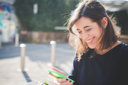 half length of a young beautiful brown hair caucasian woman in town reading book while using a smartphone looking downward, smiling - culture, technology, social network conceptの写真素材