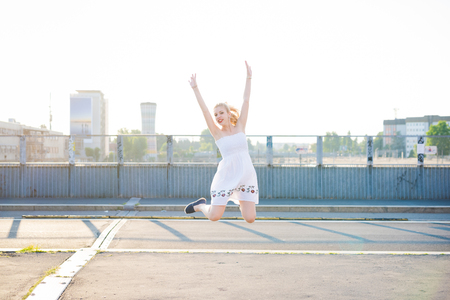 Young beautiful caucasian blonde hair woman jumping in the city backlight - goals, achievement, girl power conceptの写真素材