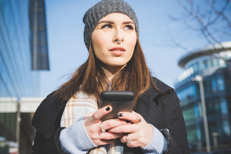 Half length of young beautiful caucasian woman holding a smartphone tapping the screen, overlooking pensive - technology, communication, social network conceptの写真素材