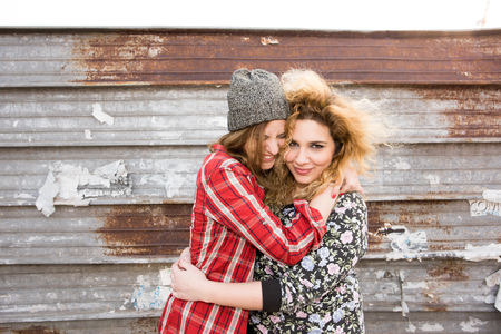Half length of two young curly and straight blonde hair caucasian woman hugging, smiling and having fun together - carefree, youthful, friendship, conceptの写真素材